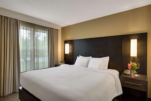 Habitación de hotel con una cama grande, cabecera oscura, dos lámparas de noche, una mesita de noche con teléfono y una ventana con cortinas.