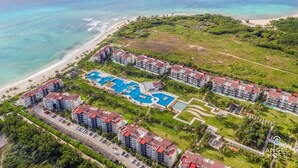 Eine Luftaufnahme eines Resorts mit mehreren Gebäuden, einem weitläufigen Poolkomplex und einem Strand.