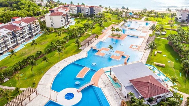 Ein Resort mit mehreren Schwimmbecken, üppiger Bepflanzung und Blick auf den Strand.