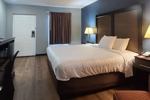 A hotel room with a large bed, bedside lamps, a desk, and a door.