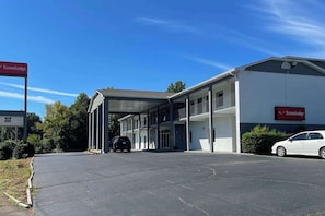 Un motel à deux étages doté d’un espace de stationnement couvert, d’une enseigne indiquant qu’il est désormais ouvert, et d’une voiture garée à l’intérieur.