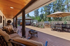 Une terrasse couverte, aménagée avec du mobilier d’extérieur, un barbecue et offrant une vue sur la forêt environnante.