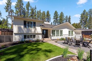 Une maison à deux étages avec une façade en pierre, un porche à l’avant et un patio aménagé avec du mobilier d’extérieur.