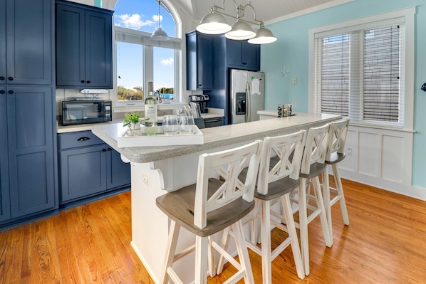 A kitchen with dark blue cabinets, a white island with bar stools, a microwave, and a refrigerator.