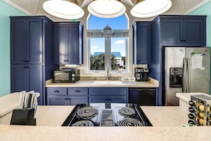 A kitchen with dark blue cabinets, a stainless steel refrigerator, a built-in microwave, a gas stove, and a coffee bar sign.