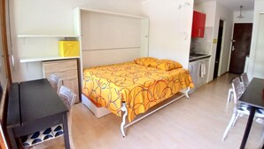 Un dormitorio compacto con una cama, un escritorio pequeño y una kitchenette.