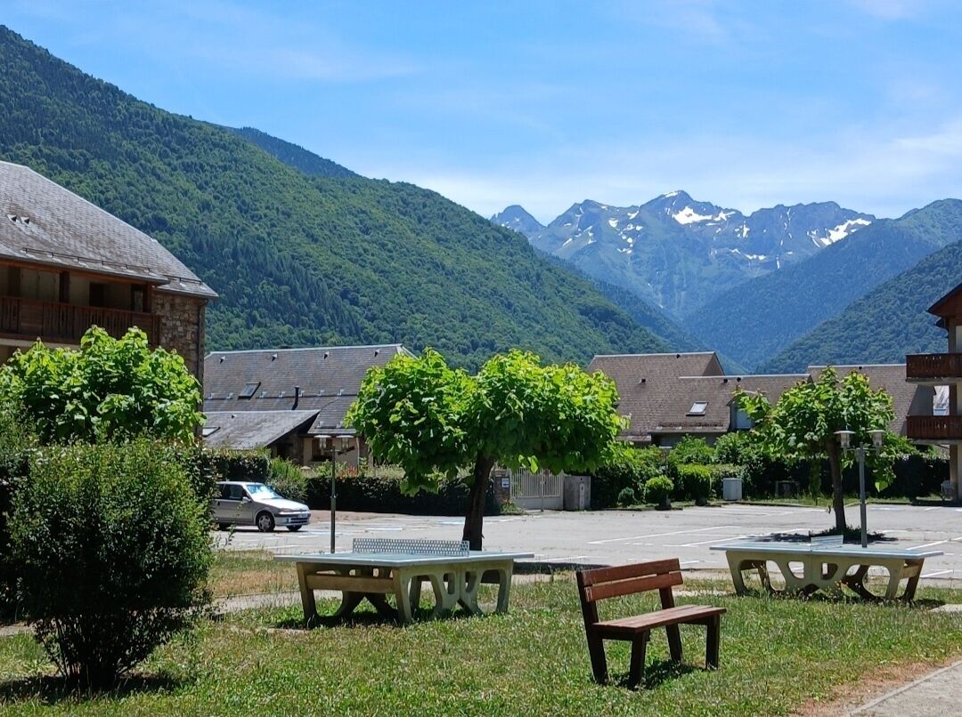 Ein Innenhof mit Picknicktischen, Bänken und einem parkenden Auto vor Gebäuden mit Blick auf die Berge.
