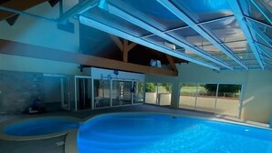 Una gran piscina coberta amb sostre de vidre, una piscina més petita a part, i una zona de terrassa amb mobiliari exterior.