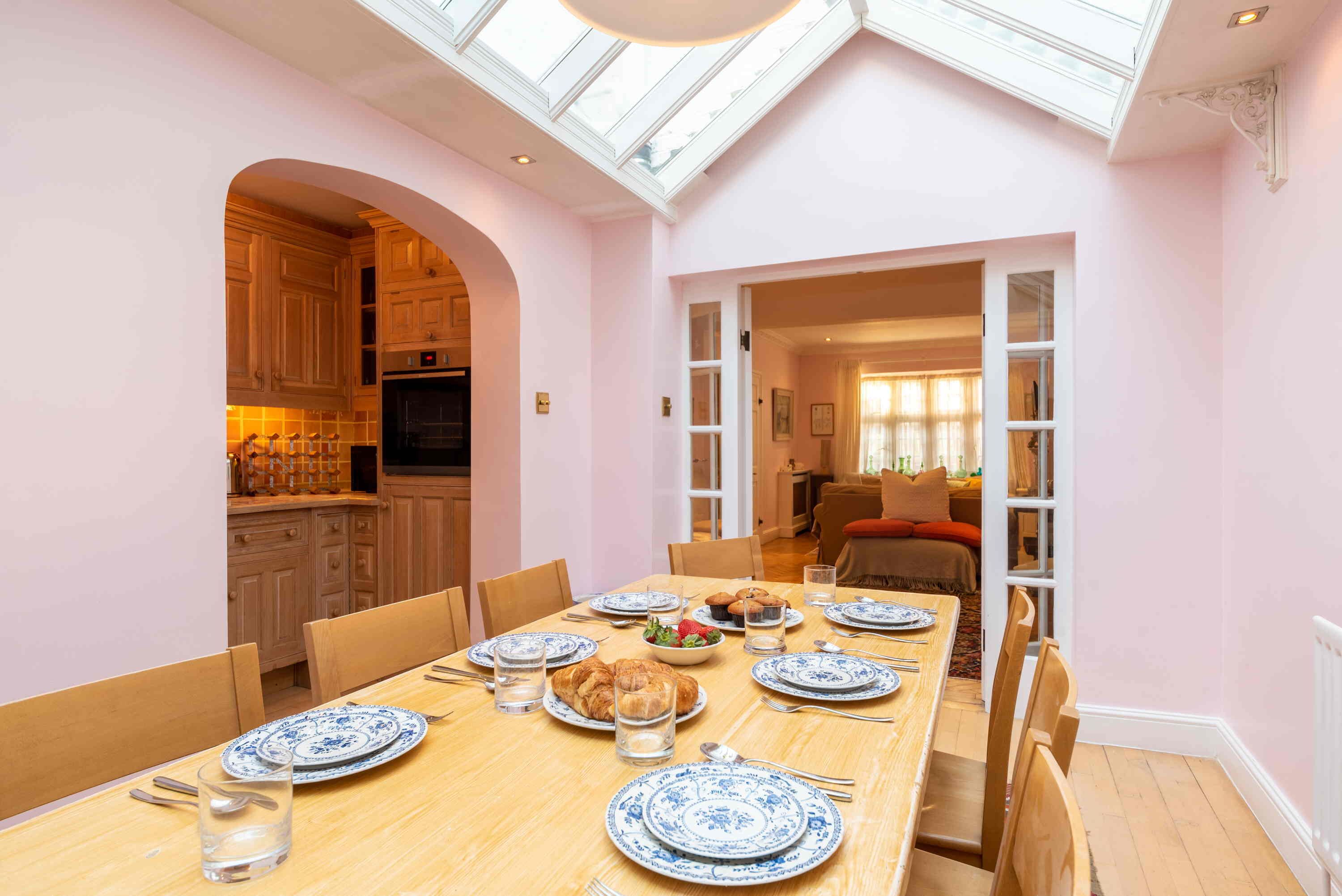 A dining area with a long table set for a meal, a kitchen with wooden cabinets, and a skylight above.