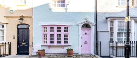 Una hilera de casas con fachadas de colores pastel, un pavimento de piedra y una valla de metal negro.