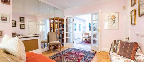 Una sala de estar con sofá, sillón y una mesita de centro. Hay una estantería y una puerta que da a otra habitación.