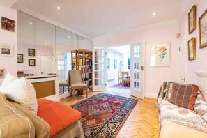 A living room with a sofa, armchair, and a coffee table. There is a bookshelf and a door leading to another room. - Godfrey Street (London)