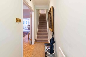 A hallway with a carpeted floor, a wooden door, a staircase, and a wall-mounted umbrella. - Godfrey Street (London)