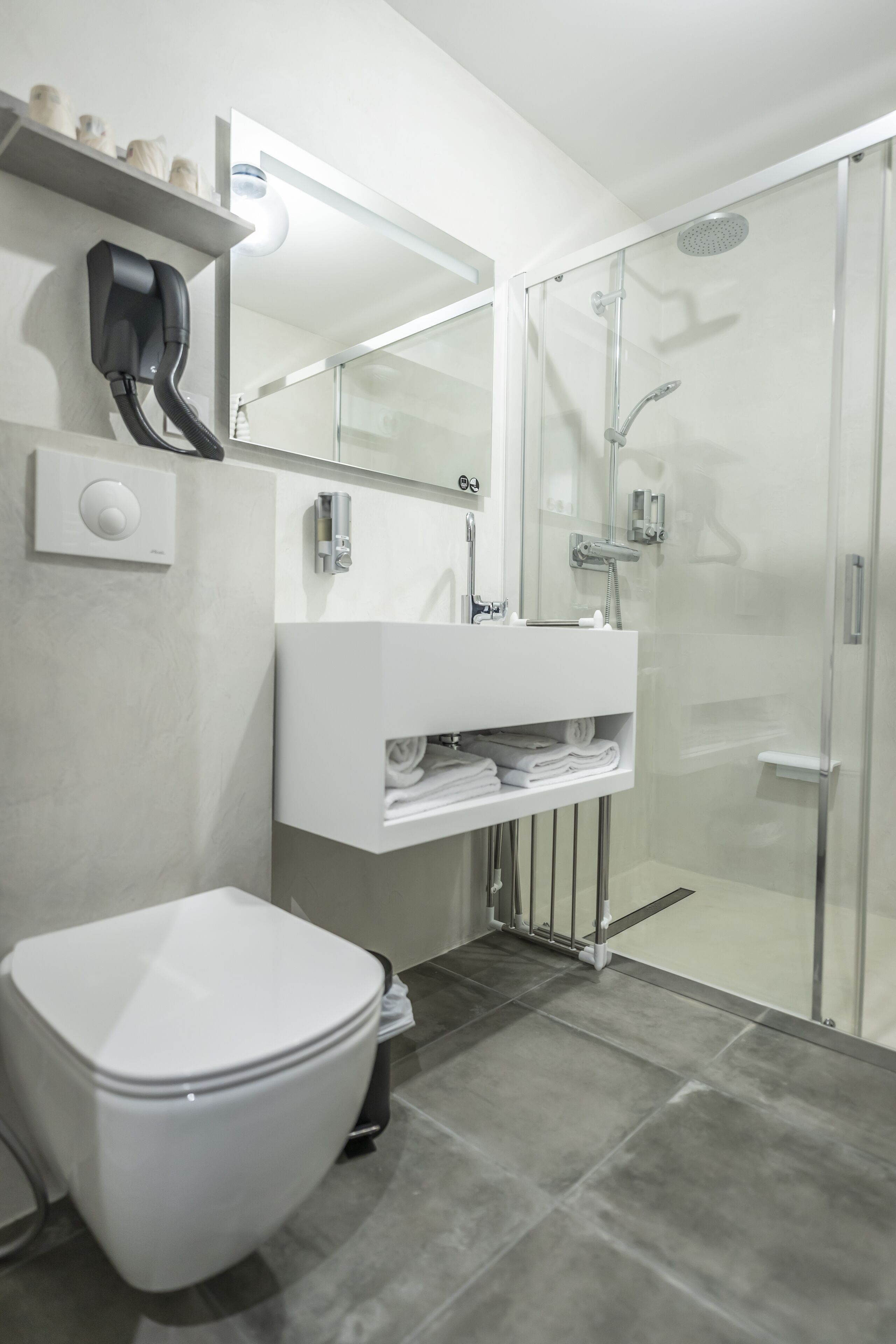 A modern bathroom with a toilet, a glass-enclosed shower, a white sink, and a mirror above the sink.