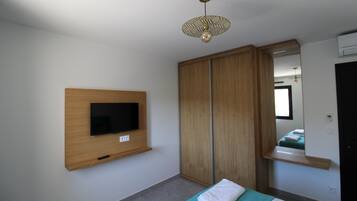 A bedroom with a TV mounted on the wall, a wardrobe, a bed with a green blanket, and a mirror above the bed.