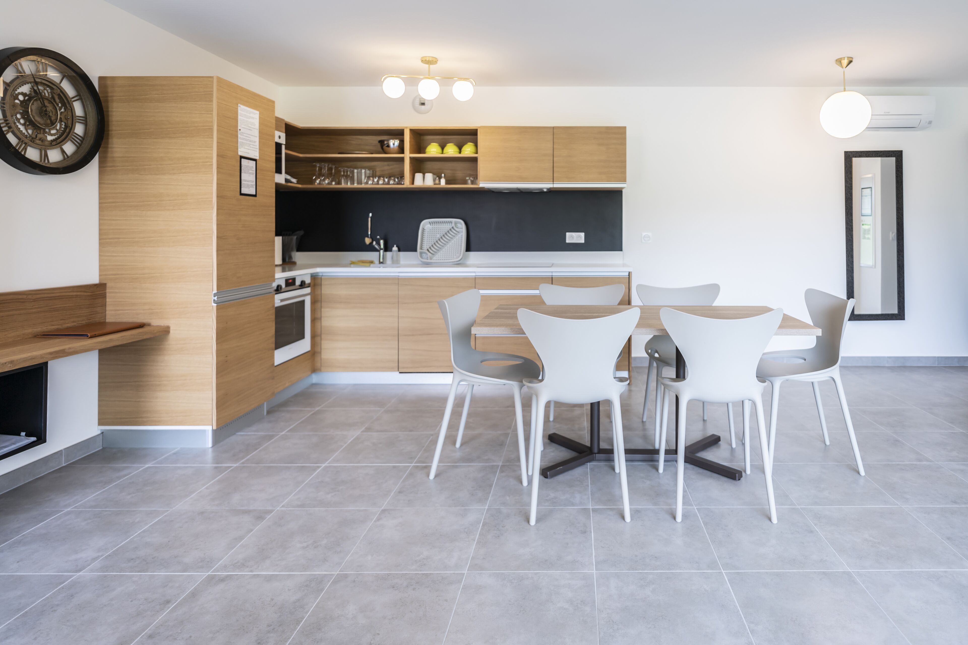 A modern kitchen with wooden cabinets, a built-in oven, and a dining area with white chairs and a round table.