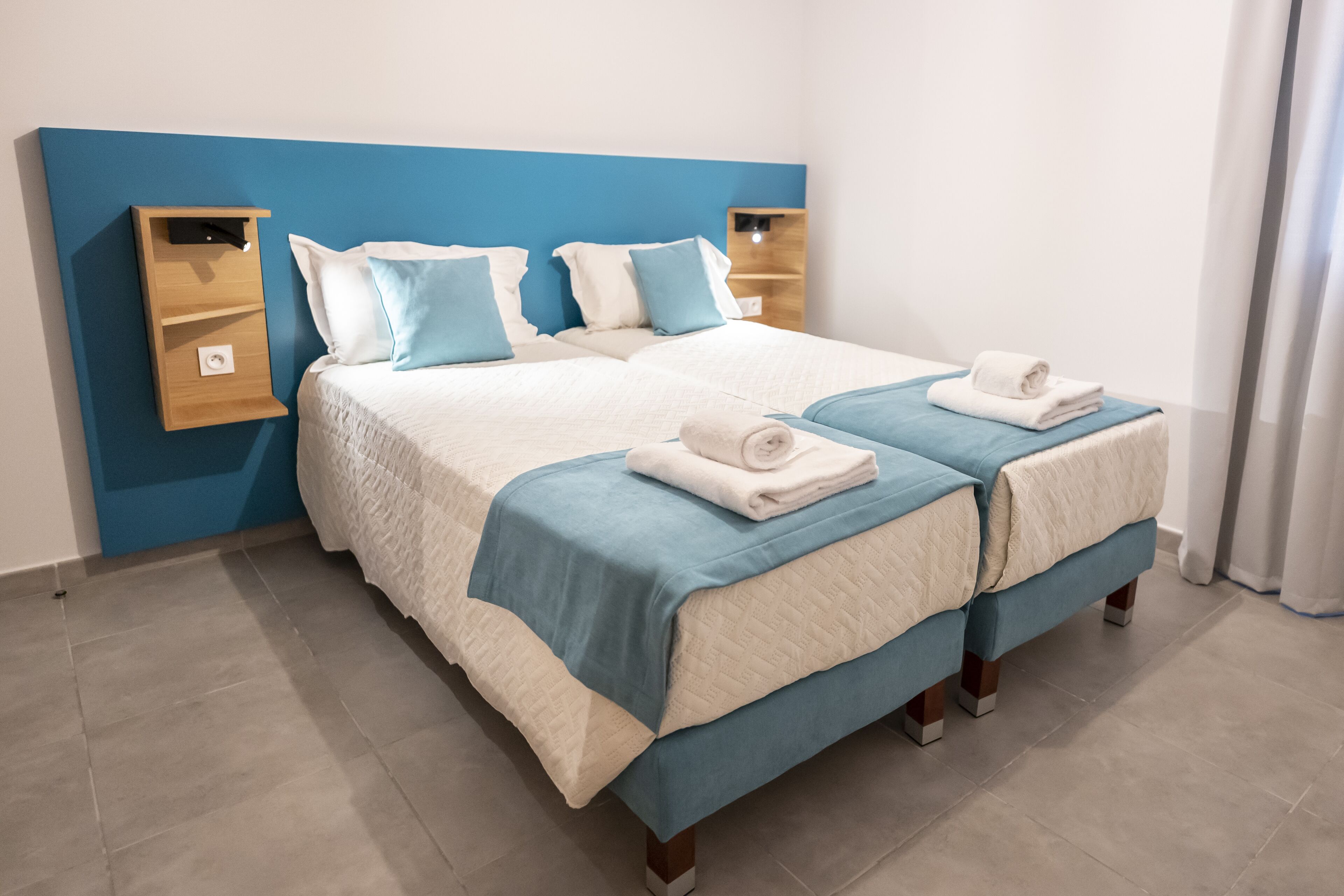 Una cama doble con cabecera azul y dos mesitas de noche, cada una con un estante.