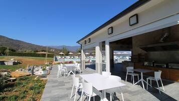 Une terrasse extérieure avec des tables et des chaises blanches, un espace piscine en arrière-plan et une vue sur les montagnes.