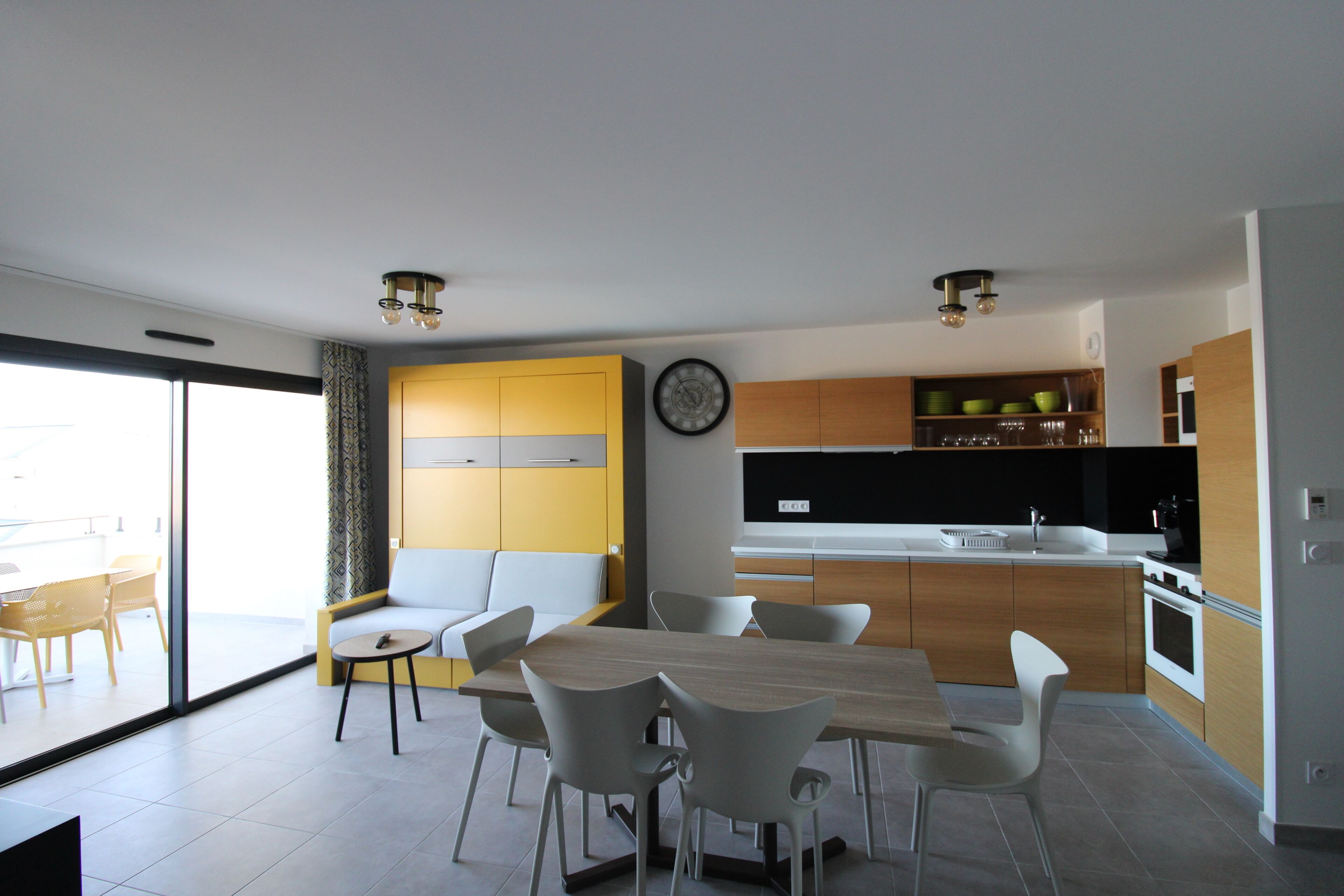 A modern kitchen with a dining area, featuring a large table, chairs, and a clock on the wall.