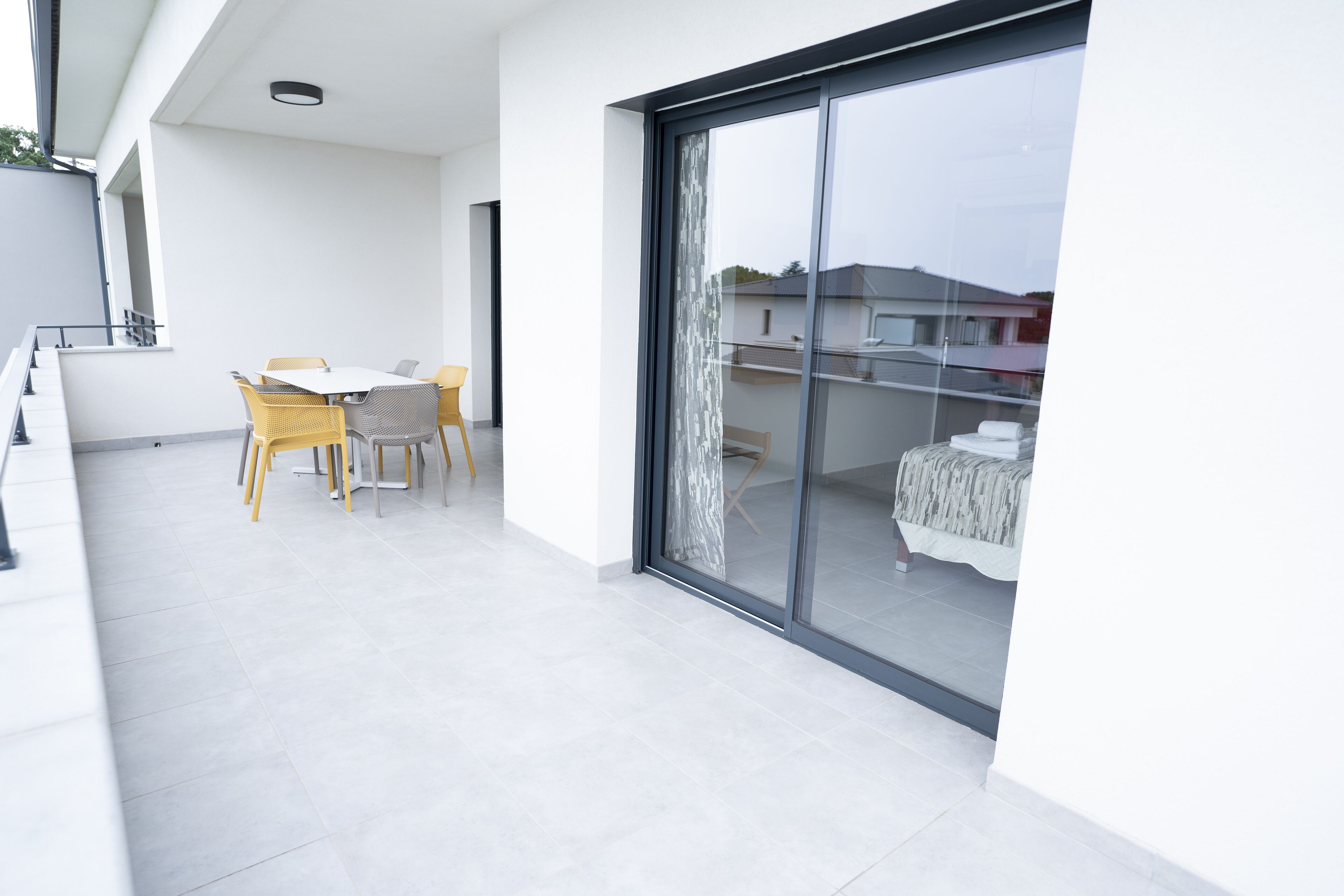Un balcón moderno con una mesa y sillas de comedor, una puerta corrediza de vidrio que da a un dormitorio y un piso de baldosas impecable.