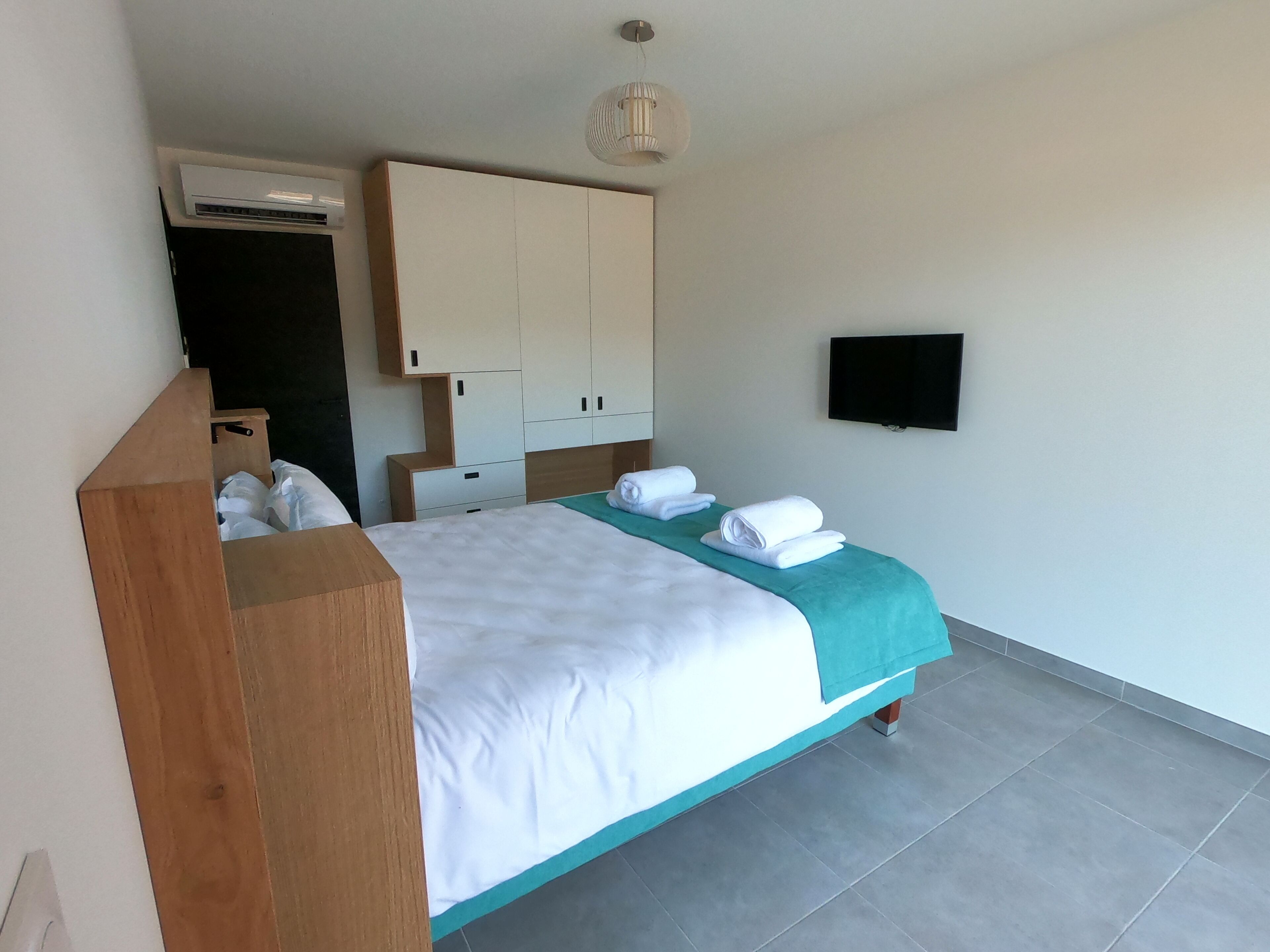 A bedroom with a bed, a wooden headboard, a TV mounted on the wall, and a ceiling fan.