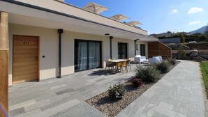 A modern building with a patio area featuring outdoor seating, a wooden door labeled "C11", and a stone pathway leading to the entrance. - Hotel Résidence a Torra (Vescovato)