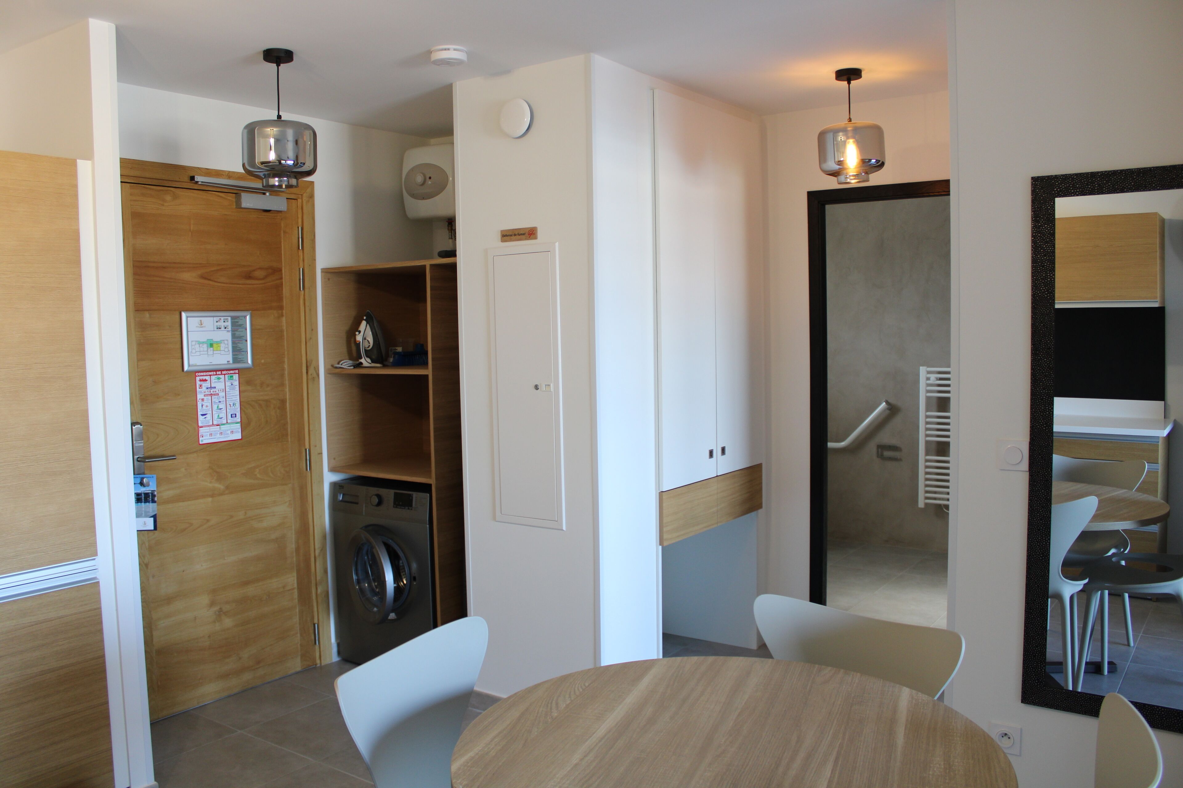 Un espace de vie compact comprenant un lave-linge, une table à manger et un miroir qui reflète l’espace repas.