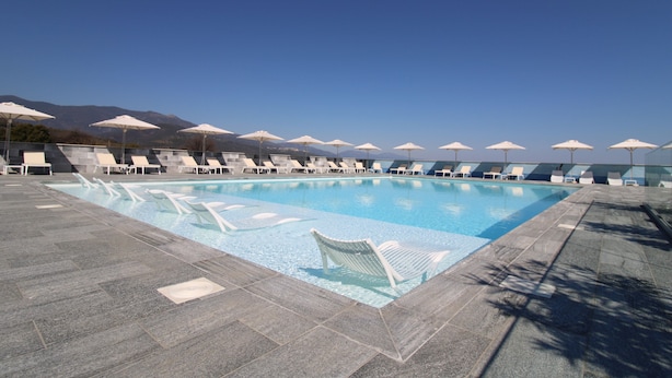 A swimming pool with lounge chairs and umbrellas, surrounded by mountains. - Hotel Résidence a Torra (Vescovato)
