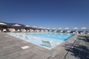 Piscina com espreguiçadeiras e guarda-sóis, rodeada por montanhas.