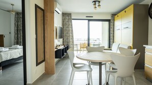 A modern hotel room with a bed, a dining table with chairs, a TV, and a balcony with a view. - Hotel Résidence a Torra (Vescovato)