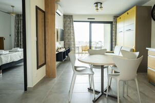 Quarto de hotel moderno com uma cama, uma mesa de jantar com cadeiras, uma televisão e uma varanda com vista.