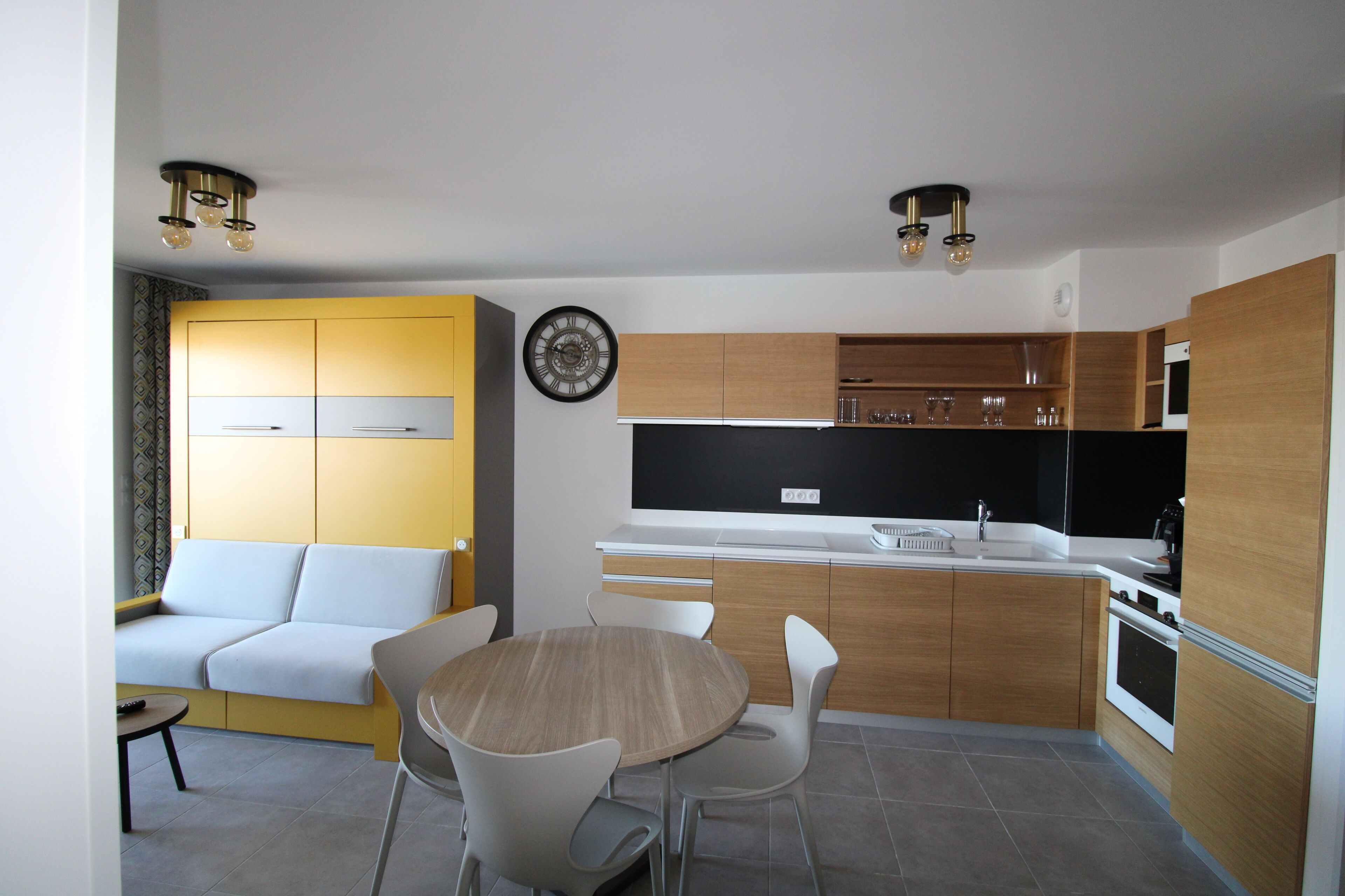 Una cocina moderna con armarios de madera, horno empotrado y comedor con una mesa redonda y sillas.