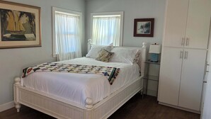 A bedroom with a white bed, a wardrobe, and a painting on the wall. - Cozy Morro Bay Bungalo (Morro Bay)