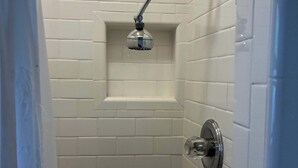 A shower with a handheld showerhead, white tiled walls, and a corner design. - Cozy Morro Bay Bungalo (Morro Bay)
