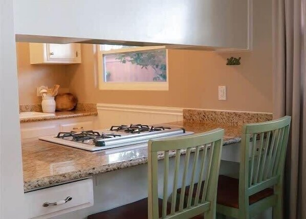A kitchen with a gas stove, wooden chairs, a window with a view, and a small cabinet.