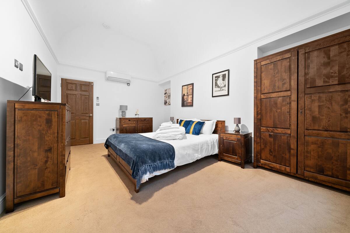 A bedroom with a large bed, wooden wardrobe, and a television.