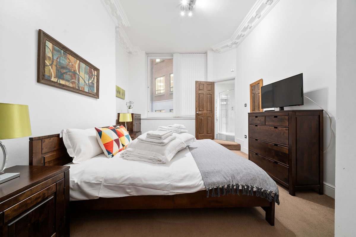 A bedroom with a bed, a TV, a dresser, and a painting on the wall.