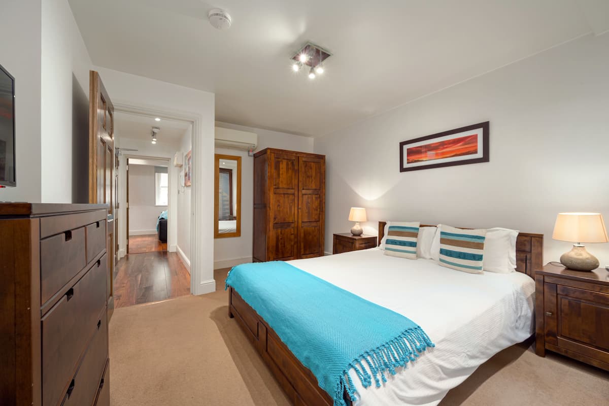A bedroom with a large bed, wooden wardrobe, and a nightstand with a lamp.