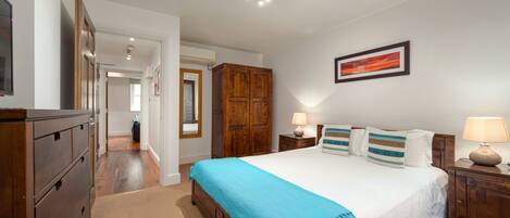 Quarto com cama grande, guarda-roupa de madeira e mesa de cabeceira com abajur.