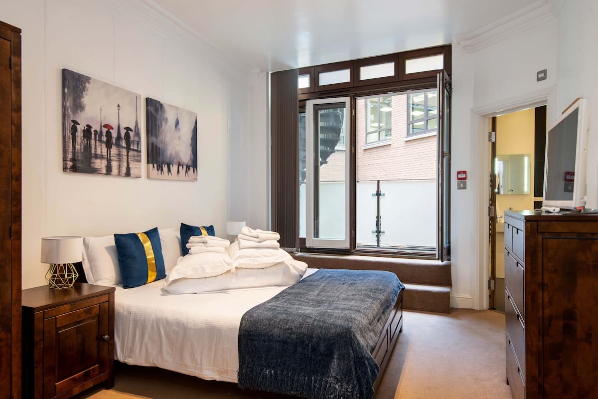 A hotel room with a bed, a nightstand, a dresser, and a window with a view of the outside.