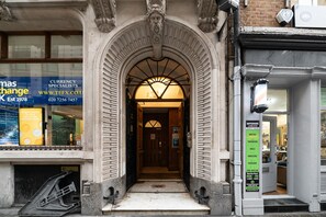 An entrance with a large archway, a sign for a currency exchange, and a salon with a sign listing services like waxing and pedicure. - 48 Bishopsgate by City Living London (London)