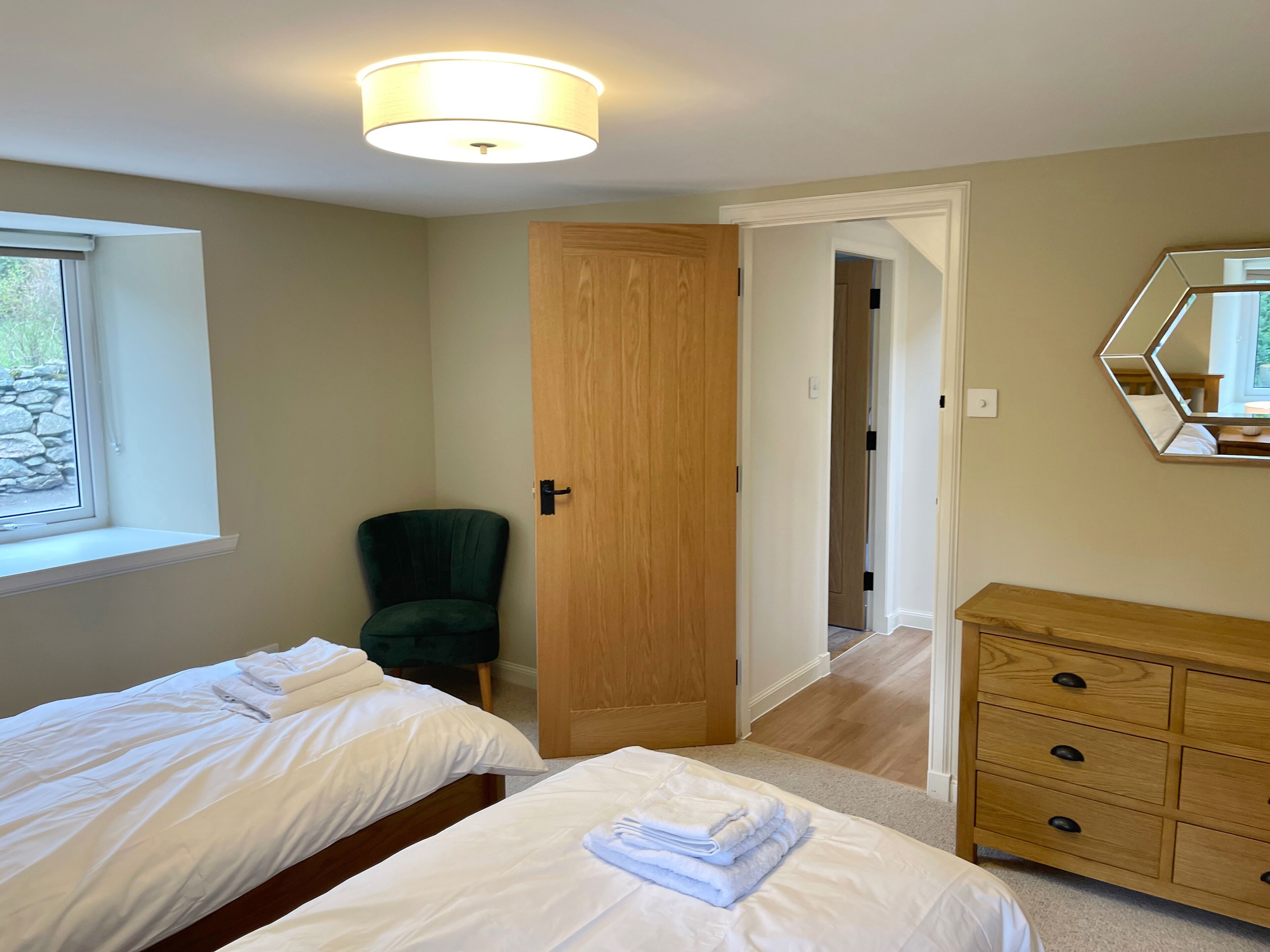 A bedroom with two beds, a wooden dresser, a chair, and a door leading to another room.