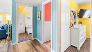 Una habitación con piso de madera, un sofá azul, un tocador blanco y una puerta que da a otra estancia.