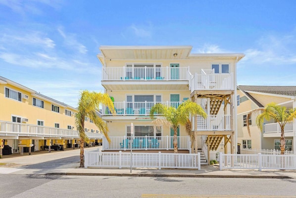 A multi-story hotel with balconies, a pool area, and a white fence.