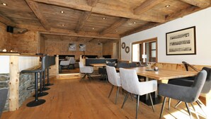 Un grand espace dédié à la salle à manger, avec une table et des chaises en bois, un coin bar avec des tabourets et un plafond rustique.
