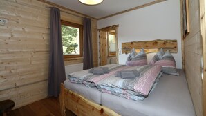 Une pièce aux murs lambrissés, avec un lit, une fenêtre avec des rideaux et un luminaire au plafond.