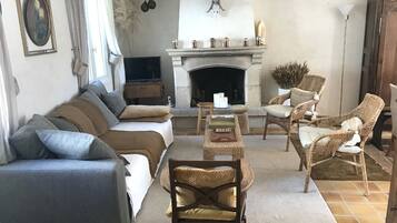 Un salon avec une cheminée, des canapés, des fauteuils en osier et un téléviseur.