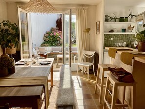 Een lichte eetruimte met een tafel voor twee personen, een bankje en uitzicht op een tuin door een glazen deur.