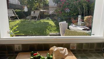 Une cuisine avec une fenêtre donnant sur un jardin arrière comprenant une pelouse, une terrasse en bois et un pot de fleurs.