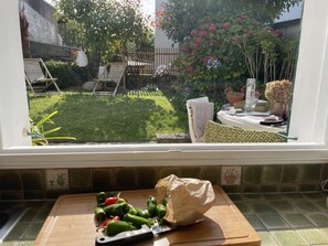 Een keuken met uitzicht op een achtertuin met een gazon, een houten terras en een potplant.